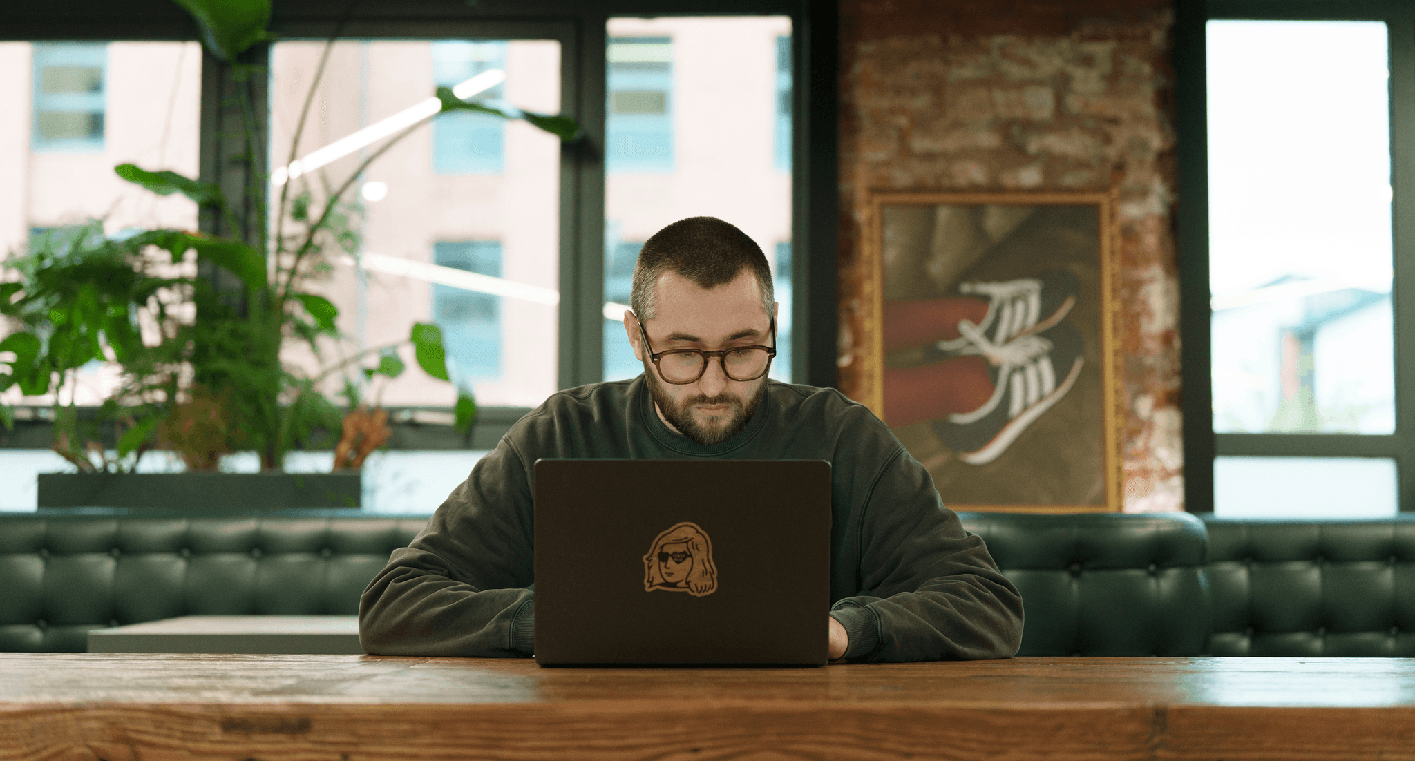 Man with glasses working on a laptop in a bright, modern studio or office environment.
